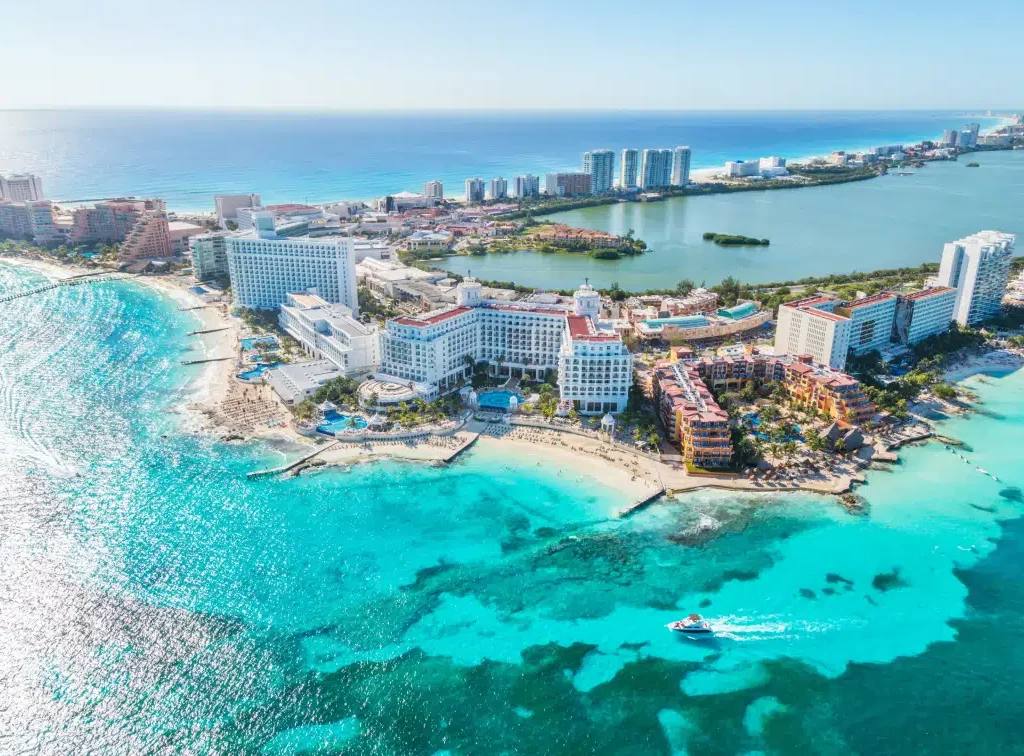 Playa de arena blanca y mar turquesa en Cancún, con palmeras y cielo azul.